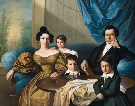 Porträt von Dr. Frušić mit seiner Frau und drei Kindern in eleganter Kleidung auf einem blauen Sitzmöbel und einem blauen Vorhang im Hintergrund