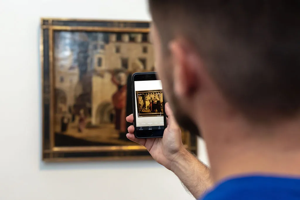 Mann steht vor einem Bild mit dem Handy in der Hand