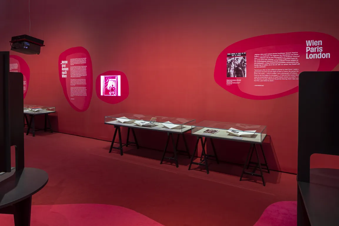 Ausstellungsraum mit roten Wänden, darauf surrealistische Bilder 