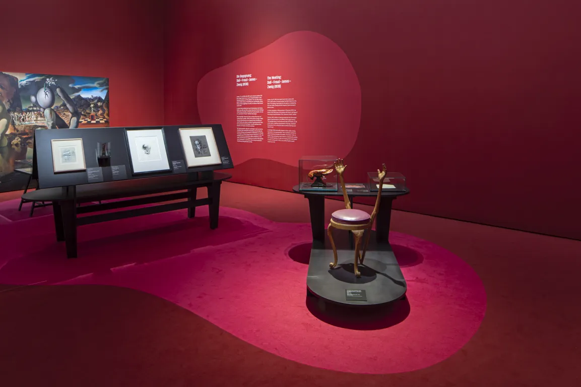 Ausstellungsraum mit roten Wänden, darauf surrealistische Bilder 