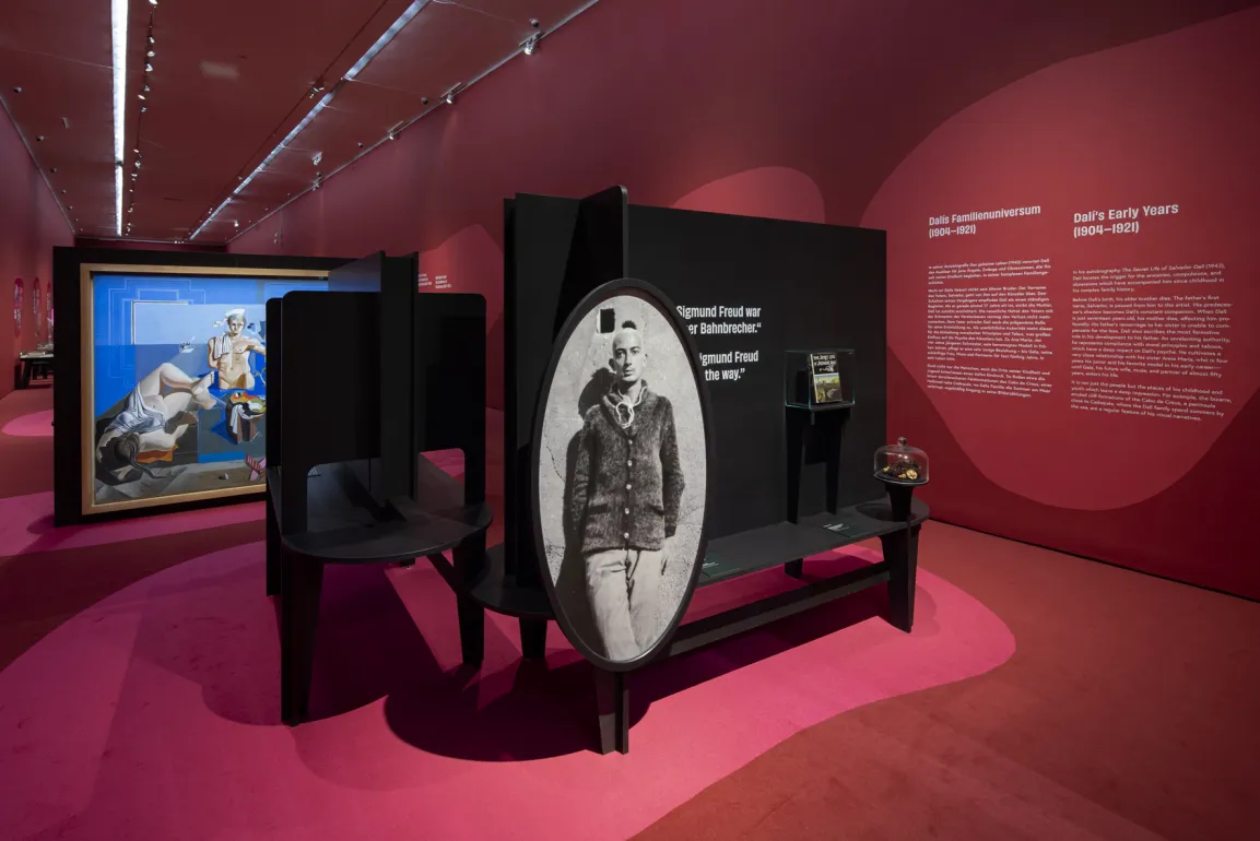 Ausstellungsraum mit roten Wänden, darauf surrealistische Bilder 