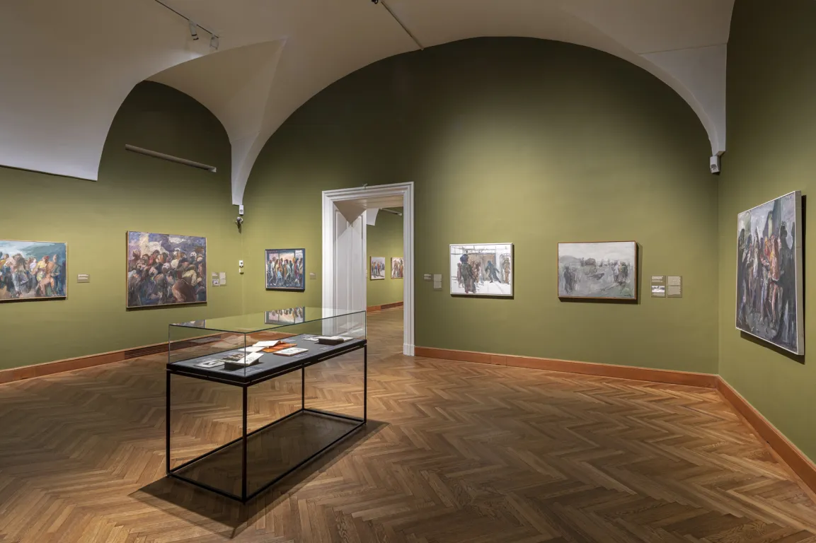 Ausstellungsraum mit gewölbter Decke und moosgrünen Wänden, darauf vage Bilder von Menschen