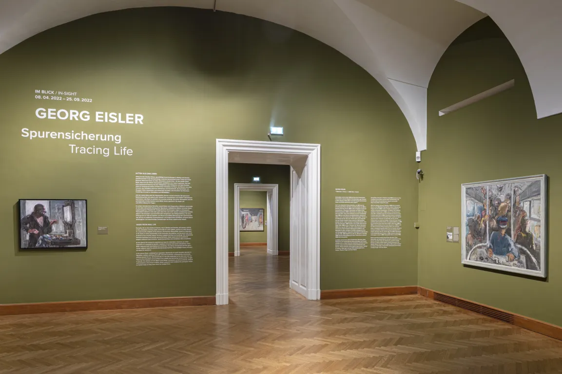 Ausstellungsraum mit gewölbter Decke und moosgrünen Wänden, darauf vage Bilder von Menschen
