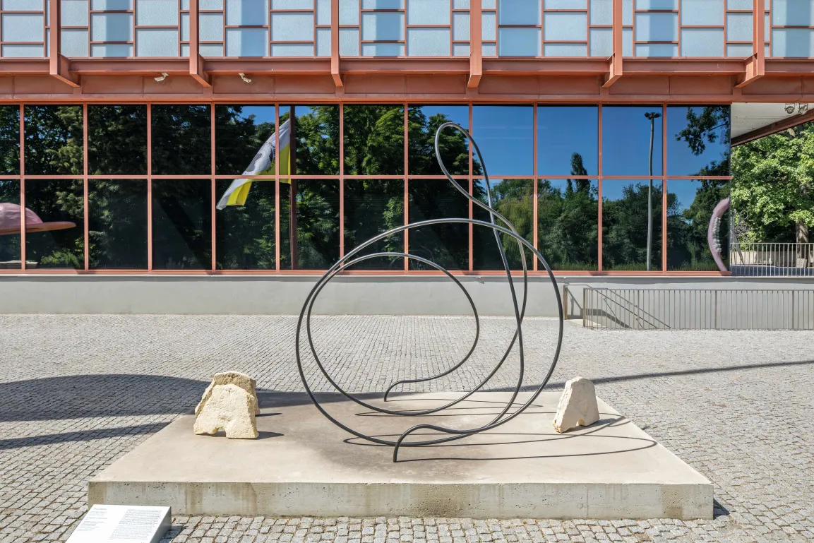 Skulptur von Carola Dertnig aus Stahlrundrohr in einer geschwungenen Form und drei Pferdeköpfen aus Mühlsteinen