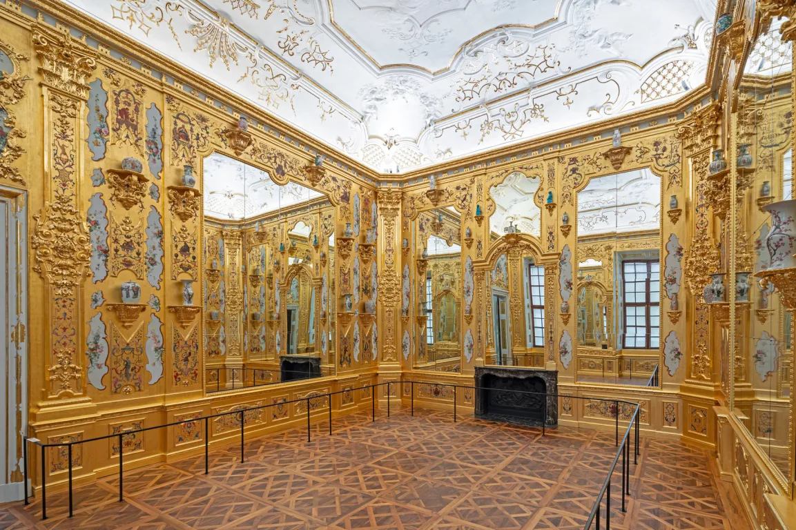A room with wooden floors, white ceiling and walls covered in mirrors and gold-leafs