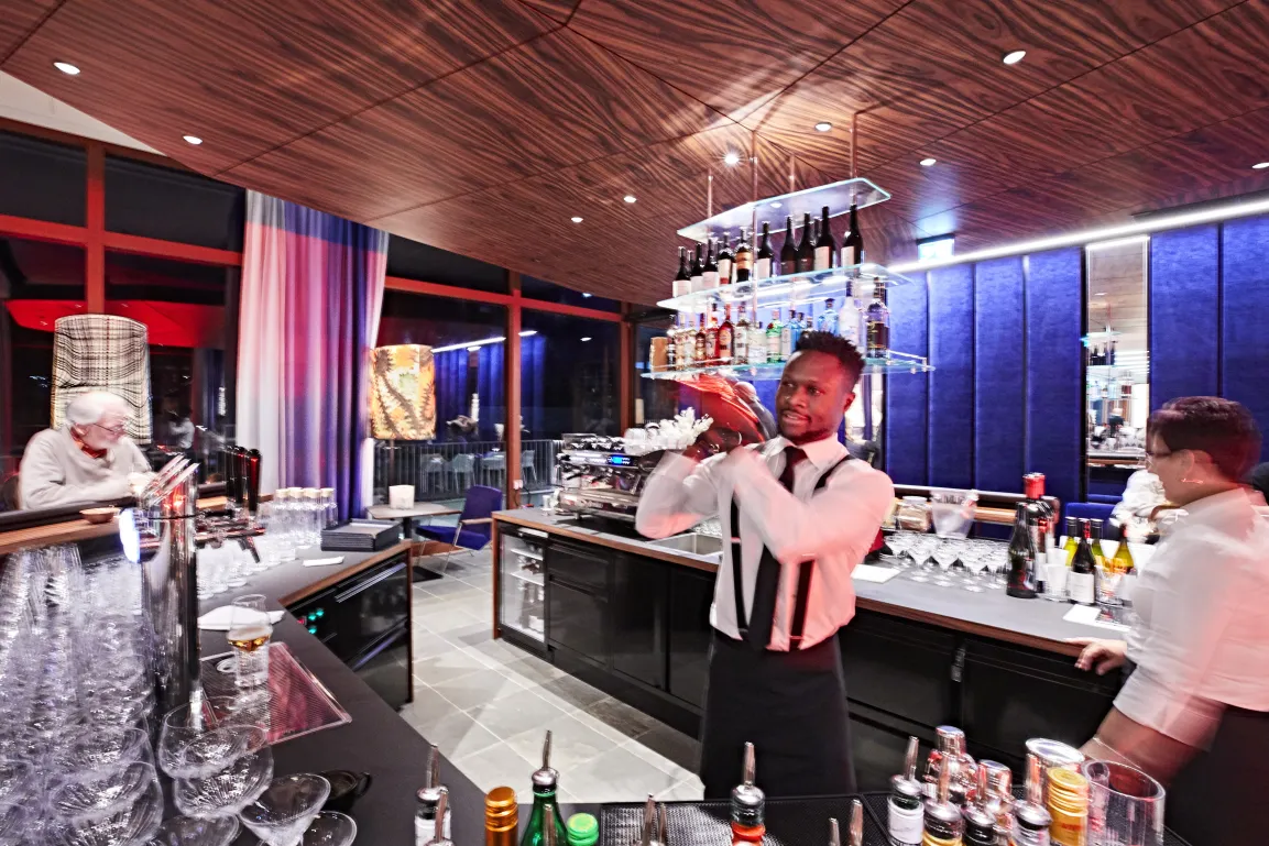 A bar within a café. A barkeeper is mixing a drink in a cocktail shaker.