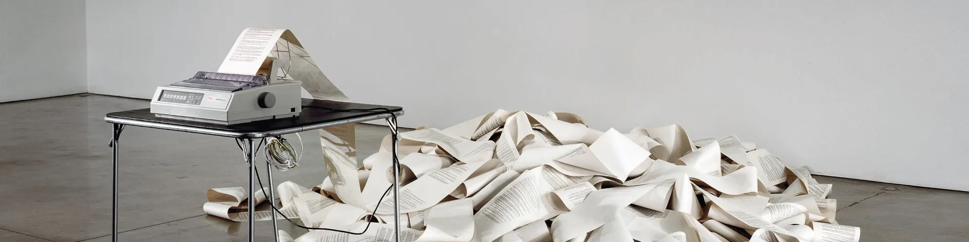 The artwork Messages (1969) consists of a fax machine on a plain metal table that continuously prints text on paper. The printed messages form a chaotic pile of paper on the floor.