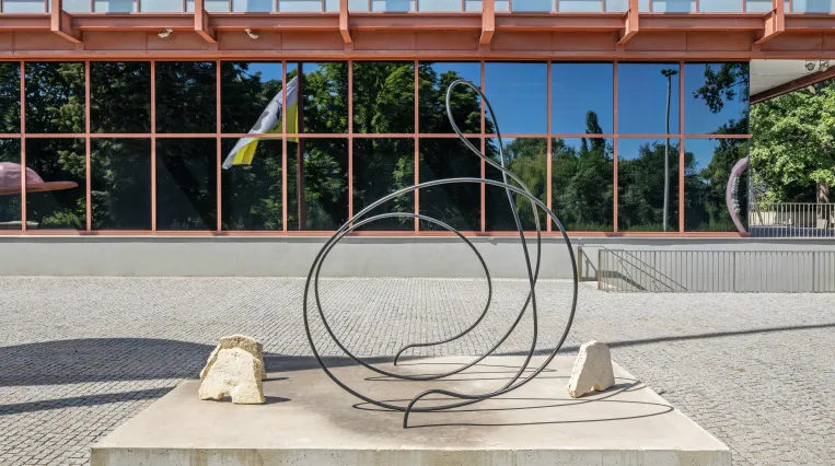 Skulptur von Carola Dertnig aus Stahlrundrohr in einer geschwungenen Form und drei Pferdeköpfen aus Mühlsteinen