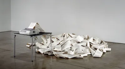 The artwork Messages (1969) consists of a fax machine on a plain metal table that continuously prints text on paper. The printed messages form a chaotic pile of paper on the floor.