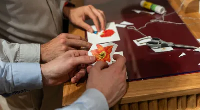 Zwei Personen bei einem Collagen Workshop mit ausgeschnittenen Fotografien in der Hand